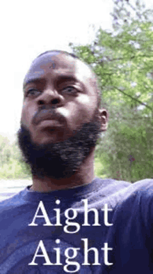 a man with a beard is wearing a blue shirt with the words `` aight aight '' written on it .