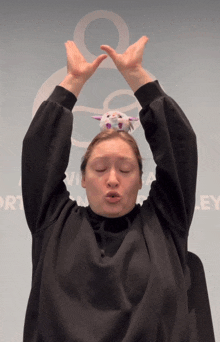 a woman in a black sweater has a stuffed animal on her head in front of a wall that says ley