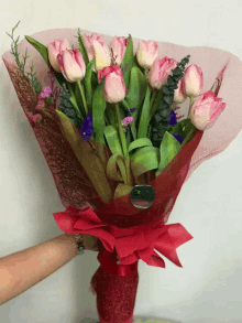 a person holding a bouquet of pink flowers with a red bow