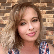 a woman stands in front of a brick wall smiling