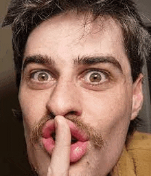 a close up of a man with a mustache holding his finger to his mouth .