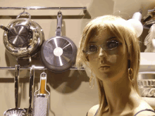 a mannequin stands in front of a wall with pots and pans hanging from it