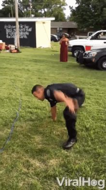 a man in a police uniform is doing push ups in the grass while a woman in a red dress looks on ..