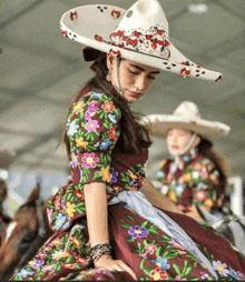 a woman wearing a sombrero and a floral dress sits on a horse