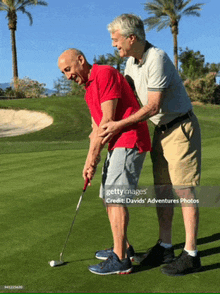 two men are playing golf on a green and one is helping the other