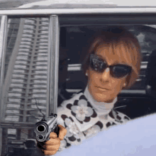 a woman wearing sunglasses is holding a gun in her hand while driving a car .