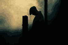 a silhouette of a man wearing a hat stands in a dark room