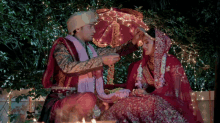 a bride and groom are sitting next to each other and the groom is holding an umbrella over the bride 's head