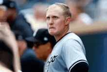 a man in a baseball uniform is standing in the dugout looking at the field .