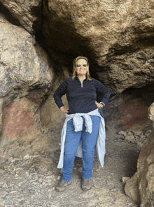 a woman wearing sunglasses and a black shirt stands in front of a large rock