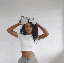 a woman wearing a crown of white flowers on her head is standing with her eyes closed in front of a white wall ..