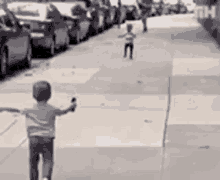 a young boy is riding a bike down a city street while another child runs behind him .