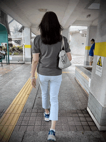 a woman walking down a sidewalk next to a sign that says ' warning '