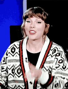 taylor swift is wearing a sweater and making a funny face while talking to the camera .