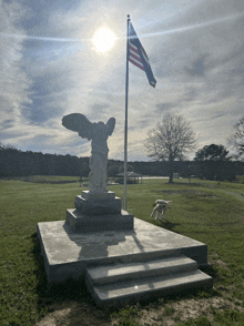 a statue of a woman with wings stands in front of a flag