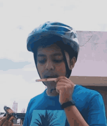 a boy wearing a helmet and a blue shirt with a pineapple on it is brushing his teeth with a toothbrush