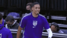 a basketball player is wearing a purple shirt and smiling while standing on a court .