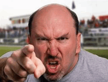 an angry bald man with a beard is pointing at the camera with his finger .