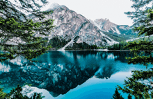 a lake surrounded by mountains and trees with a reflection of the mountains in the water