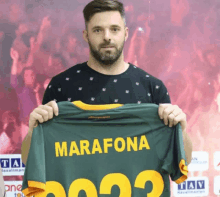 a man is holding up a green jersey with the name marafona on the back