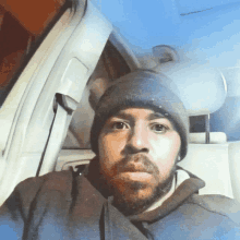 a man with a beard wearing a beanie takes a selfie in the back seat of a car