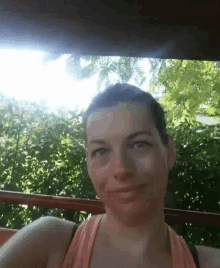 a woman with short hair is smiling for the camera while sitting on a balcony with trees in the background .