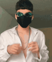 a young man wearing a mask and sunglasses is taking off his shirt