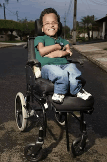 a young boy in a wheelchair with his arms crossed smiles for the camera