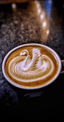 a close up of a cup of coffee with a swan design on the foam