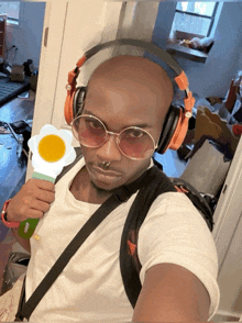 a bald man wearing headphones and sunglasses holds a flower in his hand