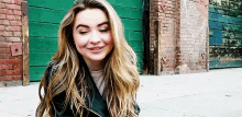 a young woman with long blonde hair is sitting on the sidewalk in front of a green garage door .