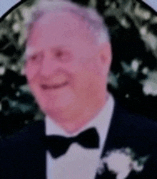 a man in a tuxedo and bow tie is smiling in a blurred photo .