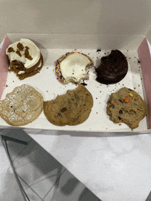 six different types of cookies are in a box with one missing a bite