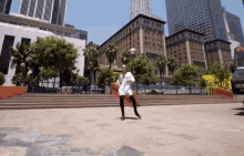 a woman in a white dress is dancing in front of a large building that says ' hollywood ' on it