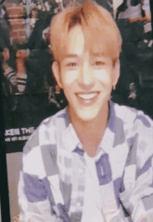 a young man in a plaid shirt smiles in front of a poster that says kiss the