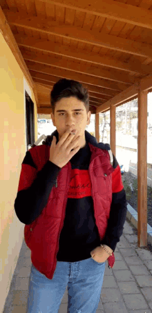 a young man wearing a red vest and a black sweater with the word california on it smoking a cigarette