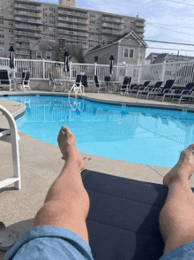 a person laying on a chair next to a pool with a building in the background