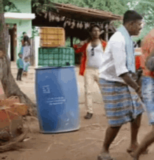 a man in a white shirt is standing next to a blue barrel that says ' ec ' on it