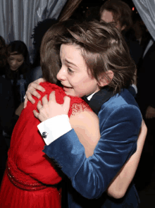 a young boy in a blue suit is hugging a woman in a red dress