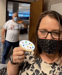 a woman wearing a mask is holding a donut with sprinkles on it