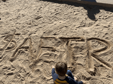 a young boy sits in the sand looking at the word safer written in the sand