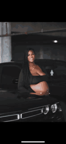 a pregnant woman is standing next to a black car in a garage .