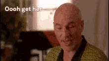 a bald man in a yellow robe is sitting in a living room with his eyes closed .