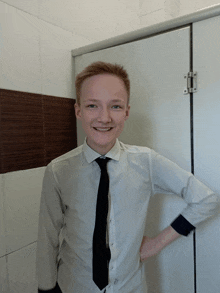 a young man wearing a white shirt and black tie stands in a bathroom stall