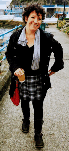 a woman wearing a black jacket and a plaid skirt is holding a cup of coffee