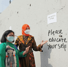 two women wearing face masks stand in front of a wall that says please educate yourself on it