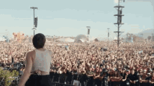 a woman in a white tank top stands in front of a crowd at a concert with the word coachella on the bottom