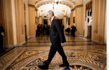 a man in a suit and red tie walks down a hallway with a mosaic floor