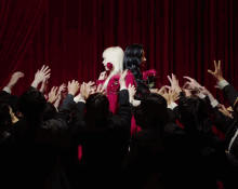 two women are standing back to back in front of a crowd of people holding roses in their hands .