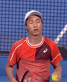 a man wearing a hat and a red shirt is standing on a tennis court with his eyes closed .